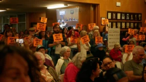 People in a crowded city hall with "ICE out of Petaluma" signs in English and Spanish